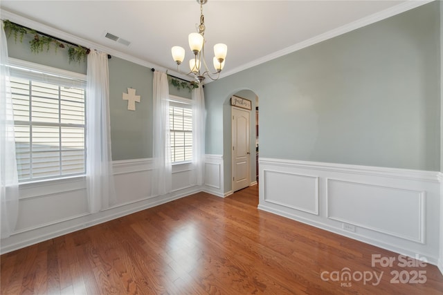 unfurnished dining area featuring visible vents, wood finished floors, arched walkways, crown molding, and a chandelier