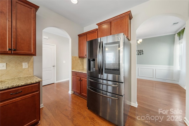 kitchen with dark wood-style floors, stainless steel fridge, light stone countertops, and arched walkways