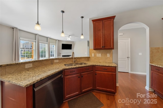 kitchen featuring dark wood-type flooring, light stone counters, stainless steel dishwasher, hanging light fixtures, and a sink