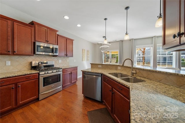 kitchen with dark wood-style floors, a sink, decorative backsplash, hanging light fixtures, and stainless steel appliances