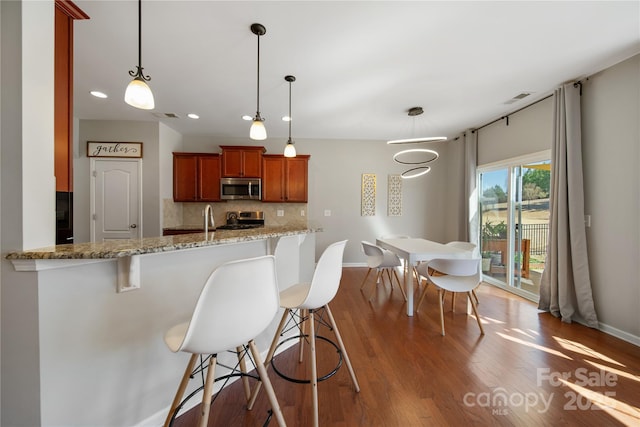 kitchen with wood finished floors, visible vents, stainless steel appliances, a kitchen breakfast bar, and tasteful backsplash