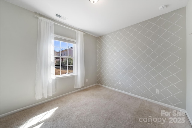 carpeted spare room featuring visible vents, baseboards, and an accent wall