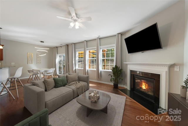 living room with a fireplace with flush hearth, ceiling fan, baseboards, and wood finished floors