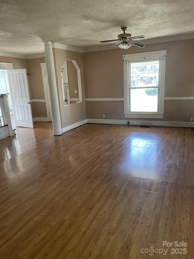 spare room with a ceiling fan, wainscoting, crown molding, and wood finished floors