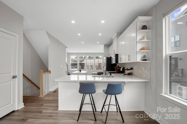 kitchen with open shelves, tasteful backsplash, stainless steel microwave, white cabinetry, and light wood-type flooring