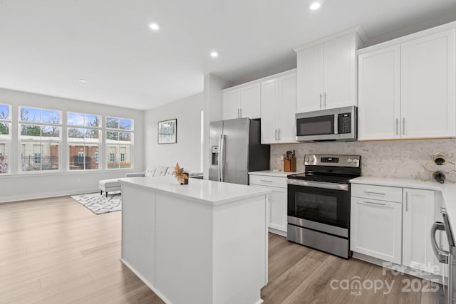 kitchen featuring light wood-style flooring, appliances with stainless steel finishes, decorative backsplash, and a center island