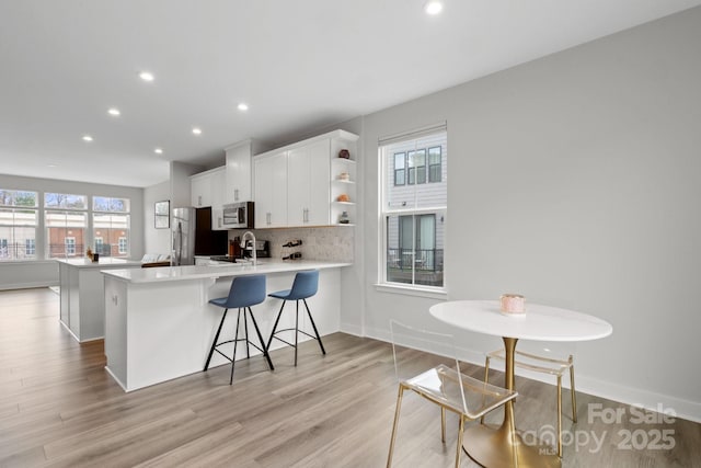 kitchen with open shelves, tasteful backsplash, light wood-style flooring, appliances with stainless steel finishes, and white cabinetry