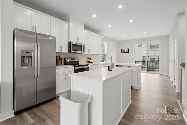 kitchen featuring dark wood-style flooring, stainless steel appliances, light countertops, a kitchen island, and a peninsula