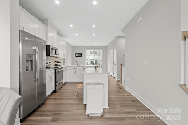 kitchen with recessed lighting, stainless steel appliances, white cabinets, backsplash, and light wood finished floors