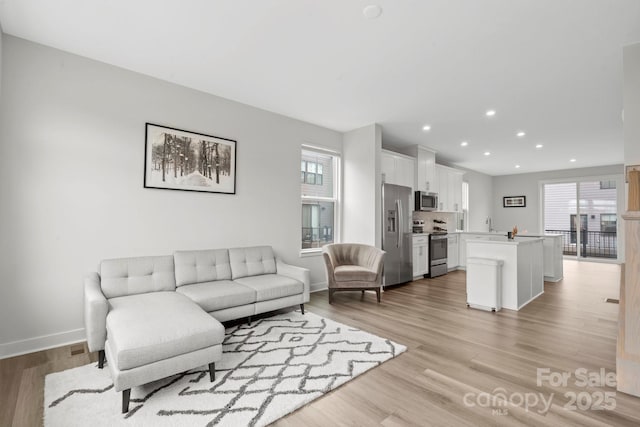 living area with light wood-type flooring, baseboards, and recessed lighting