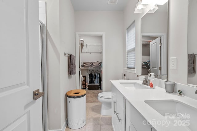 bathroom with a shower with door, a spacious closet, a sink, and tile patterned floors