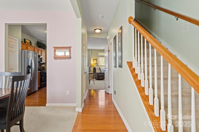 hallway with baseboards, light wood-style floors, light carpet, and stairs