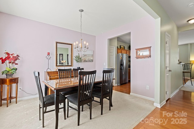 dining area featuring a chandelier, light carpet, and baseboards