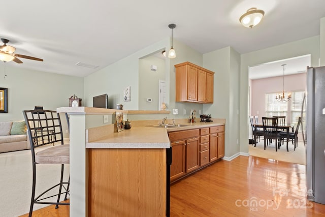 kitchen featuring open floor plan, light countertops, ceiling fan with notable chandelier, freestanding refrigerator, and a sink