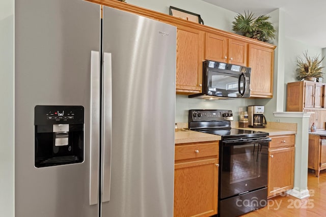 kitchen featuring light wood-type flooring, black appliances, and light countertops