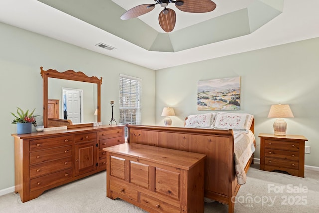 bedroom featuring visible vents, light carpet, a tray ceiling, baseboards, and ceiling fan