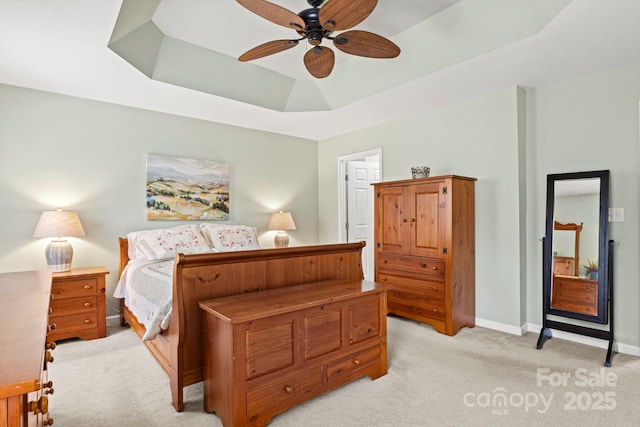 bedroom with a ceiling fan, a raised ceiling, light colored carpet, and baseboards