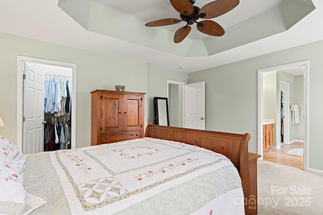 carpeted bedroom with a walk in closet, baseboards, ceiling fan, a closet, and a raised ceiling