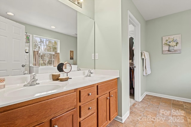 bathroom with double vanity, a spacious closet, baseboards, and a sink