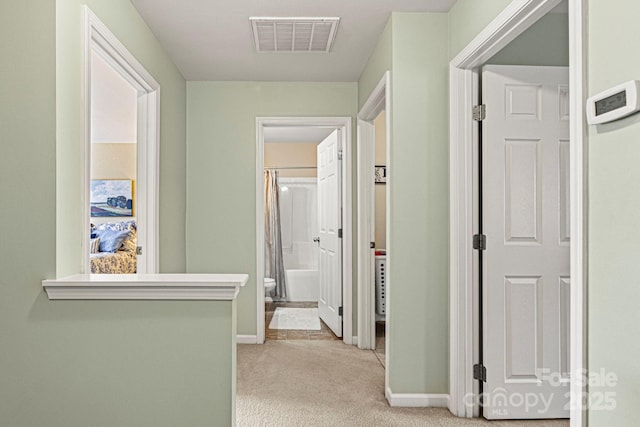 corridor with visible vents, light colored carpet, and baseboards