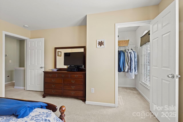 bedroom featuring a walk in closet, light colored carpet, a closet, and baseboards