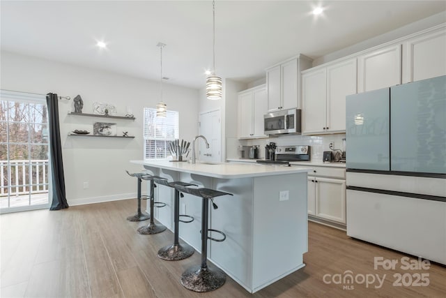 kitchen with tasteful backsplash, a sink, stainless steel appliances, white cabinetry, and a kitchen island with sink