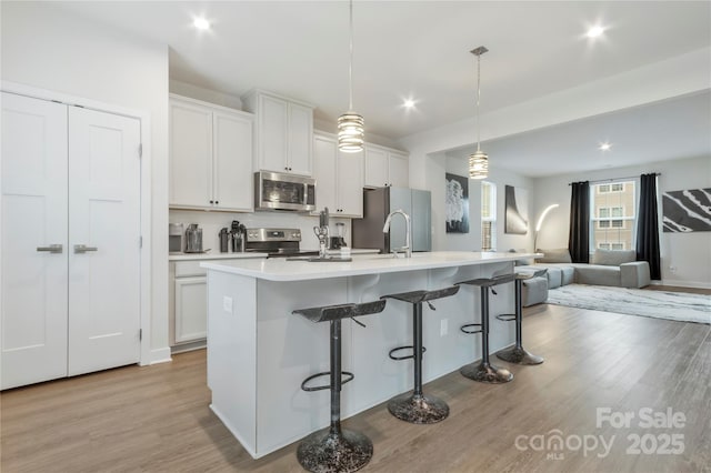 kitchen featuring light wood finished floors, open floor plan, a breakfast bar, an island with sink, and appliances with stainless steel finishes