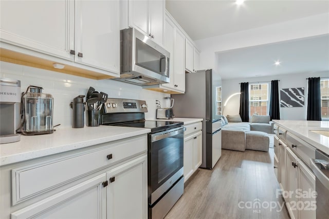 kitchen with open floor plan, white cabinetry, light wood-style floors, appliances with stainless steel finishes, and decorative backsplash