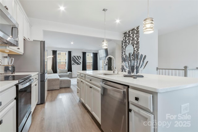 kitchen featuring a sink, stainless steel appliances, white cabinets, light wood-style floors, and open floor plan