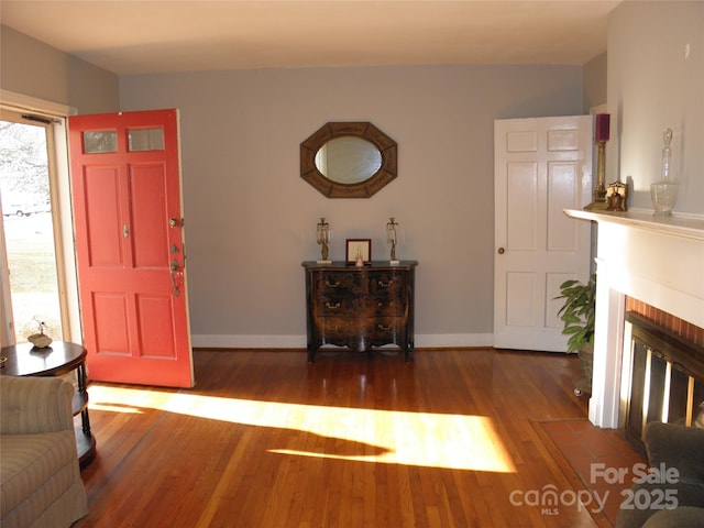 foyer entrance featuring a fireplace, wood finished floors, and baseboards