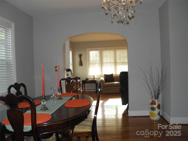 dining area featuring baseboards, arched walkways, a chandelier, and wood finished floors