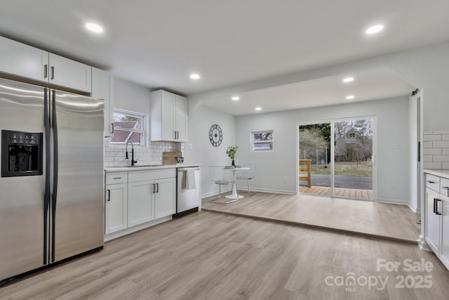 kitchen featuring light wood finished floors, decorative backsplash, appliances with stainless steel finishes, light countertops, and a sink