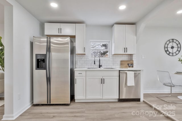 kitchen featuring a sink, white cabinetry, light wood-style floors, appliances with stainless steel finishes, and decorative backsplash