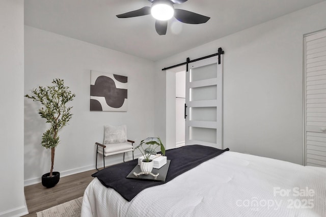 bedroom featuring a barn door, baseboards, ceiling fan, and wood finished floors