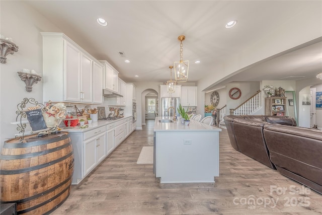 kitchen with under cabinet range hood, open floor plan, light countertops, arched walkways, and white cabinets