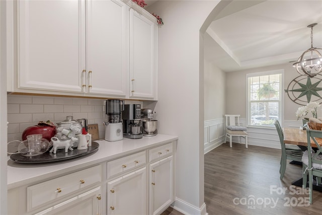 bar featuring a notable chandelier, wood finished floors, arched walkways, wainscoting, and decorative backsplash