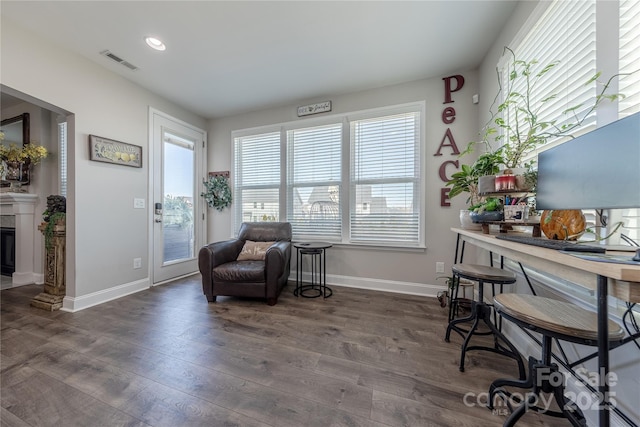 sitting room with a glass covered fireplace, wood finished floors, visible vents, and baseboards