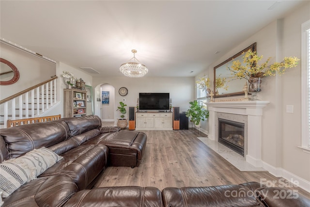 living area featuring a notable chandelier, wood finished floors, stairway, arched walkways, and a premium fireplace