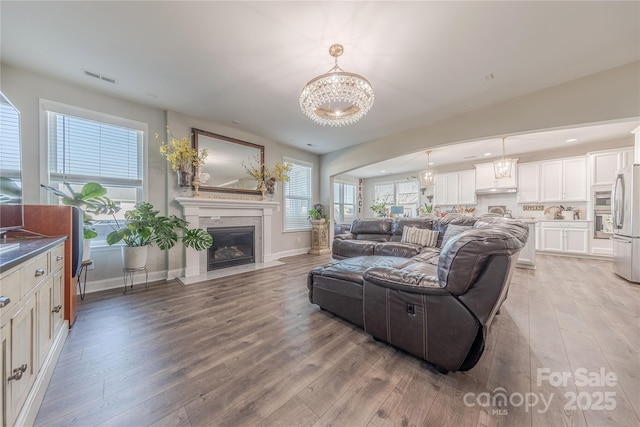 living area featuring visible vents, light wood-style flooring, an inviting chandelier, and a premium fireplace