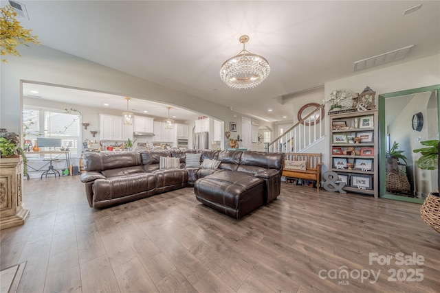 living area featuring stairs, an inviting chandelier, wood finished floors, and visible vents