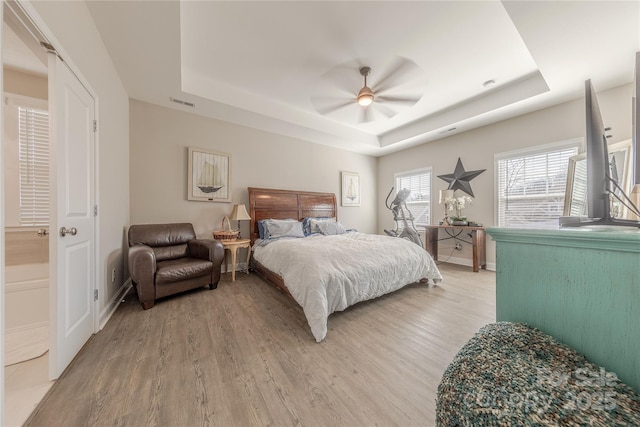 bedroom with baseboards, visible vents, ceiling fan, light wood-style floors, and a raised ceiling