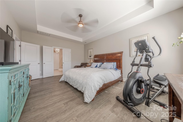 bedroom with visible vents, a raised ceiling, ceiling fan, and wood finished floors