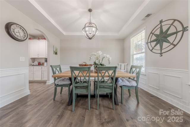 dining area featuring dark wood finished floors, a raised ceiling, visible vents, and an inviting chandelier