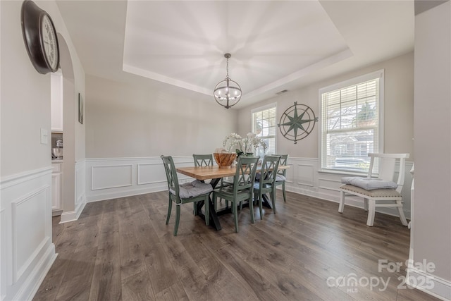 dining room with visible vents, a tray ceiling, dark wood finished floors, a decorative wall, and a chandelier