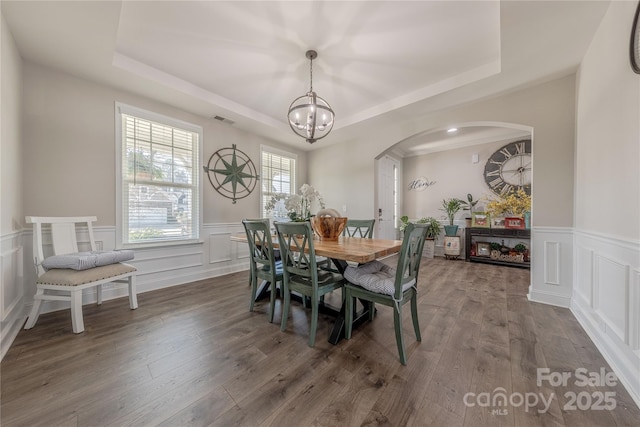 dining room with visible vents, an inviting chandelier, wood finished floors, arched walkways, and a raised ceiling