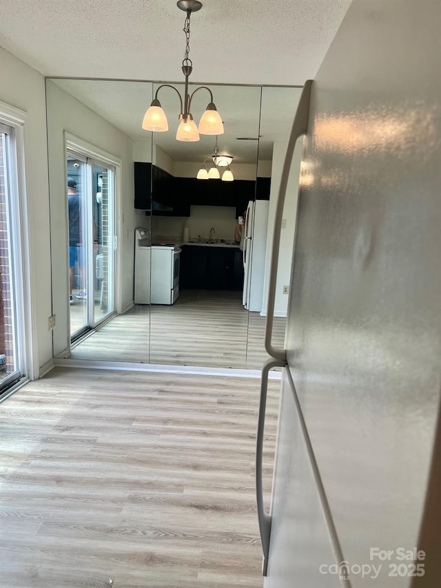 unfurnished dining area featuring a textured ceiling, light wood-style floors, a healthy amount of sunlight, and a sink
