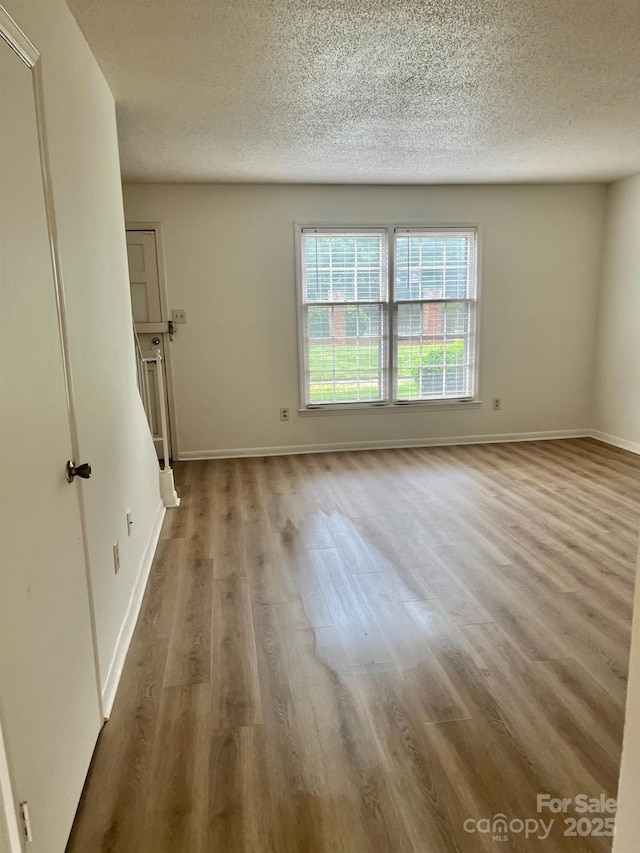 empty room with baseboards, a textured ceiling, and wood finished floors