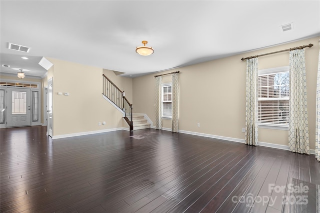 unfurnished living room with visible vents, baseboards, dark wood-style flooring, and stairway