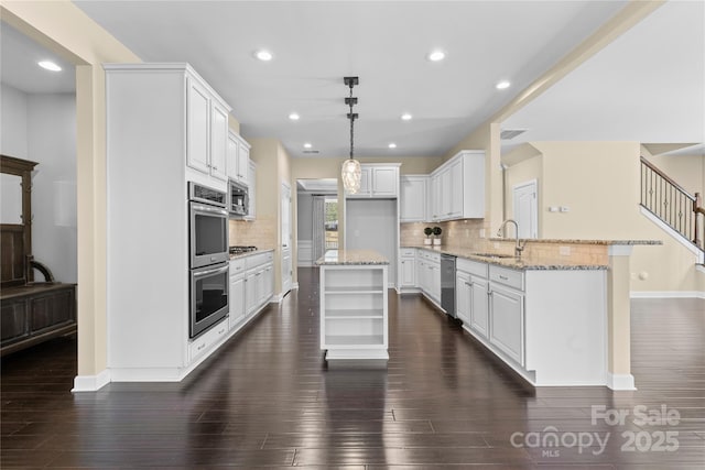 kitchen featuring open shelves, light stone counters, a peninsula, stainless steel appliances, and a sink
