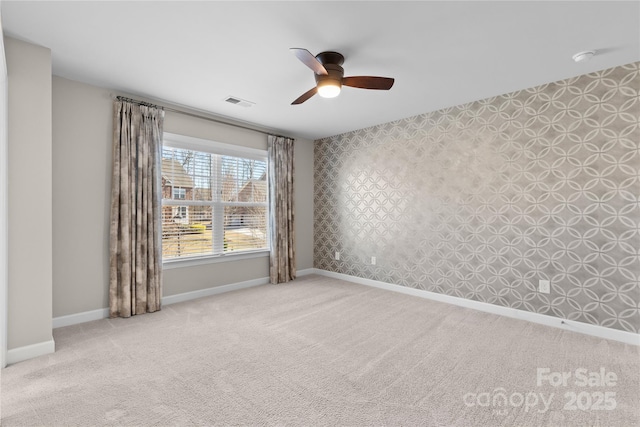 spare room with visible vents, wallpapered walls, baseboards, carpet floors, and a ceiling fan